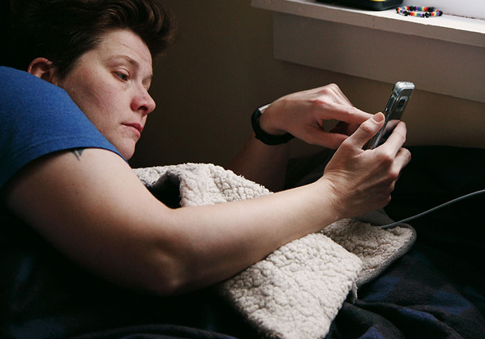 Parent lying in bed using a phone, potentially discussing teen clubbing pickup plans.