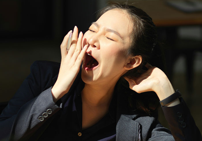 Woman yawning, covering mouth with hand, symbolizing tiredness after late-night event.