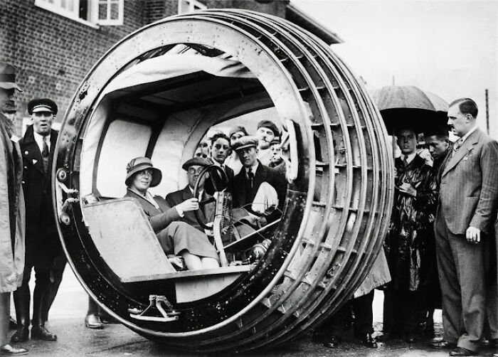 A group gathers around an early cylindrical vehicle, showcasing historical inventions ahead of their time.