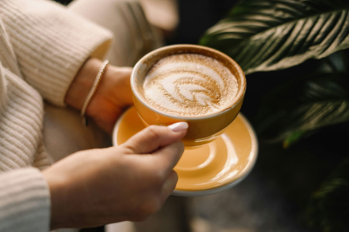 Person holding a latte in a warm ceramic cup, surrounded by soft ambient light, capturing a touching moment.