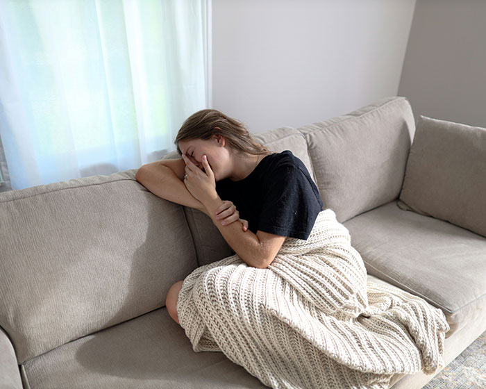 Person on a sofa under a blanket, appearing emotional, embodying touching moments shared by others.