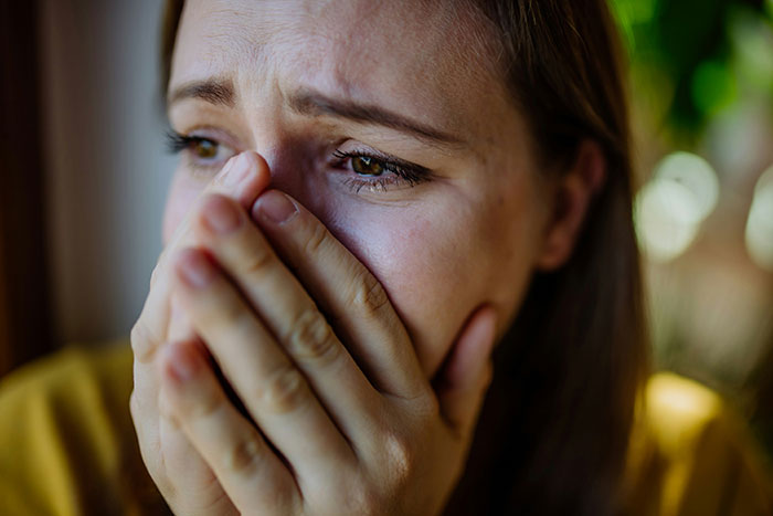 A person with tears in their eyes, moved by someone else's touching words, covering their mouth with their hands.