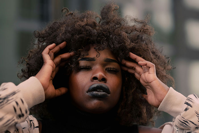 Person with curly hair and dramatic makeup, expressing a thoughtful emotion.