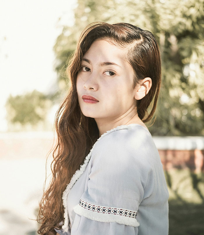 Young woman outdoors, embodying touching emotions, with long hair and thoughtful expression in natural light.