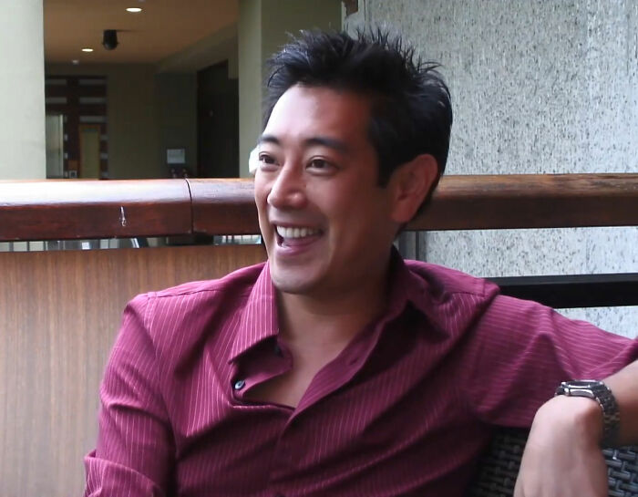 Smiling person in a red shirt, seated indoors, connected to shared reflections on impactful celebrity deaths.