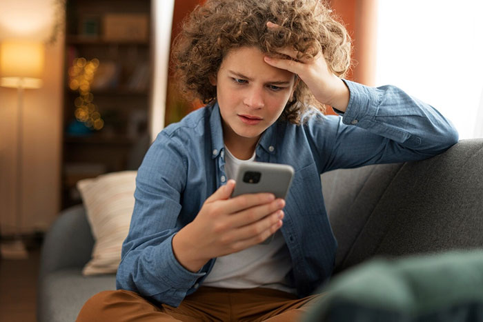 Young person on a couch, looking stressed while reading a message on a smartphone about toxic mom and inheritance.