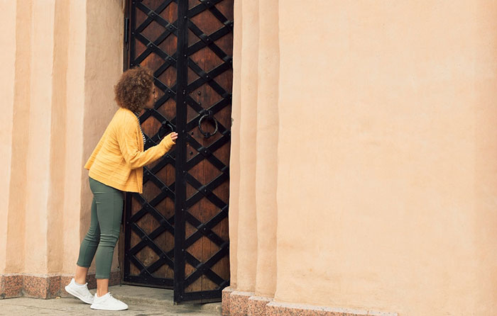 Woman in a yellow jacket at a large gate, symbolizing unexpected family visits and inheritance issues.