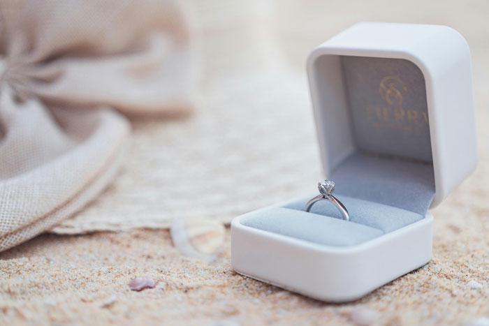 A family heirloom ring in an open box resting on sandy beach.