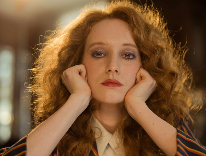 Woman with curly hair, resting her face on hands, wearing a striped jacket, reminiscent of mother-family-heirloom-ring theme.