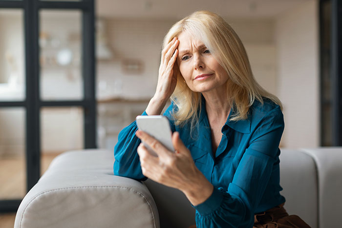 Woman looking concerned at her phone, reflecting on family issues with children abroad.