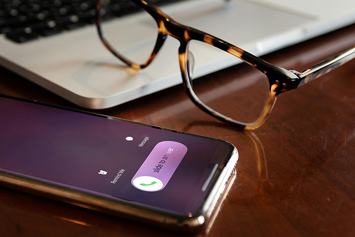 Smartphone with incoming call on a table near glasses and a laptop, illustrating blocked communication issues.