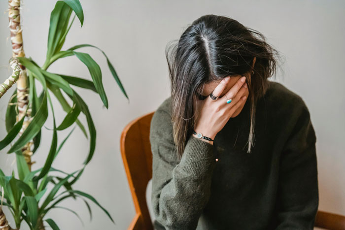 Woman sitting with hand on face, feeling upset next to a potted plant.