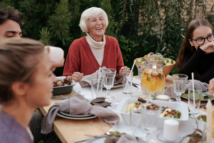 Grandma at a family dinner table, smiling while surrounded by food and drinks, discussing her cooking.