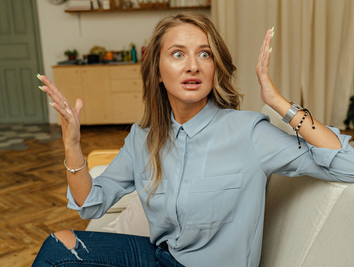 Woman looking shocked, sitting on a couch, possibly reacting to a man's mysterious disappearance.