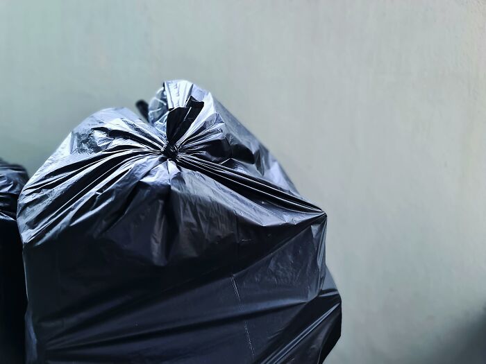 Black trash bags piled against a wall, highlighting neighbor's bin.