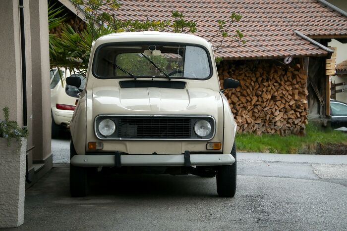 Vintage car parked beside a house with stacked wood in the background.