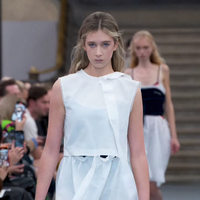 Blonde model walking runway in a white dress, embodying nepo baby success in the fashion industry.