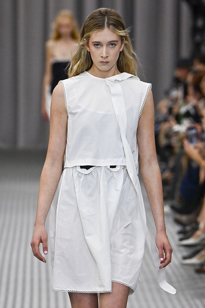 Young model in a white dress on the runway, showcasing the latest fashion trend.