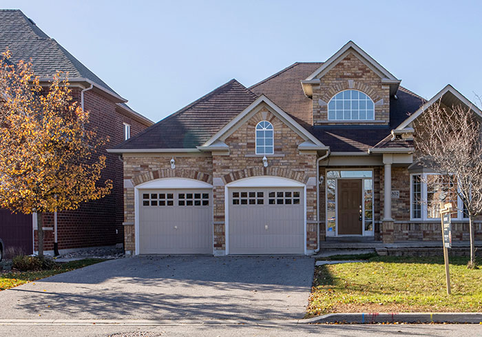 Brick house with two garages, typical in US neighborhoods, under a clear blue sky, highlighting American suburban architecture.