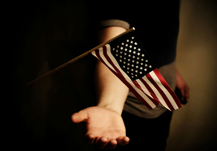 A US citizen holding an American flag against a dark background, symbolizing cultural norms.