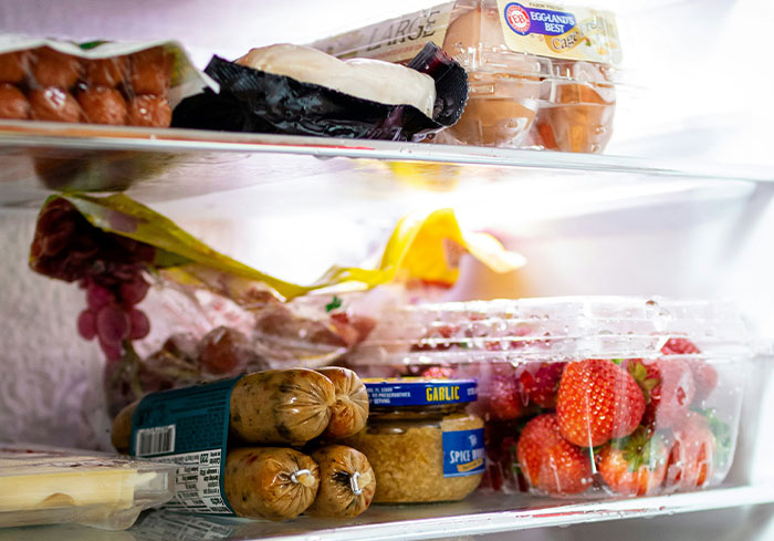 A refrigerator shelf filled with various foods common in the US, including eggs, sausages, and fresh strawberries.