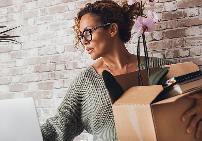 Woman with glasses holding a box and a plant, representing normal American lifestyle nuances.