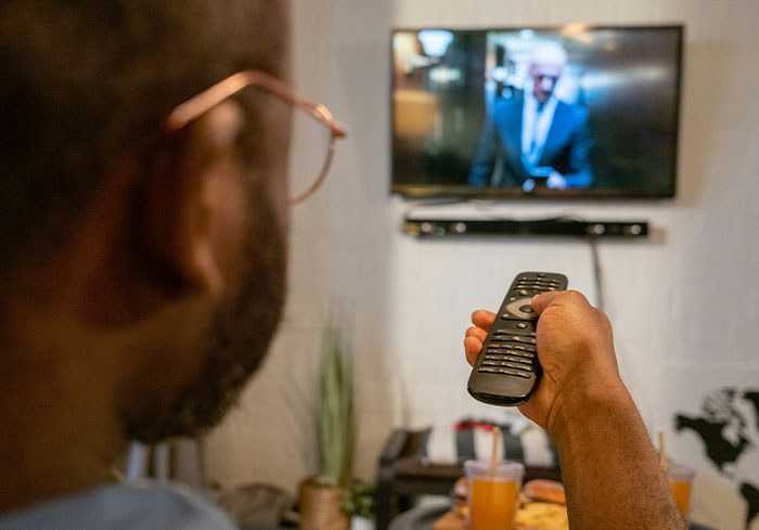 A person watching TV, holding a remote, illustrating a common activity for US citizens.