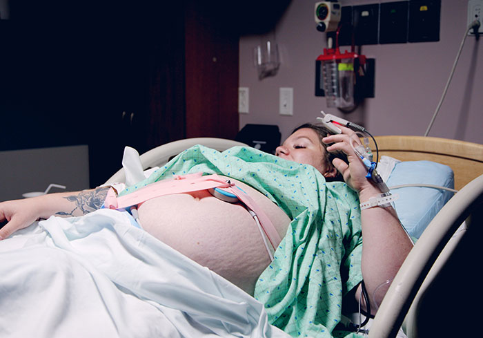 A woman in an American hospital bed, wearing a medical gown, illustrates normal US childbirth practices.