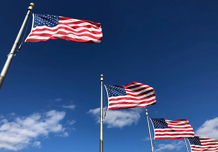 American flags waving under a clear blue sky, illustrating cultural norms familiar to US citizens.