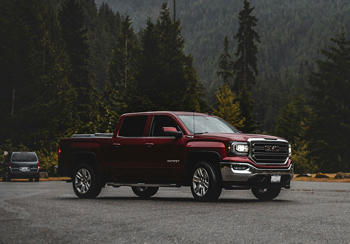 A red pickup truck parked on a road surrounded by lush green forest, representing something normal to US citizens.