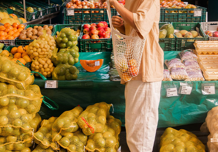 Person shopping with a net bag at a grocery store filled with fruits, illustrating a common American practice.