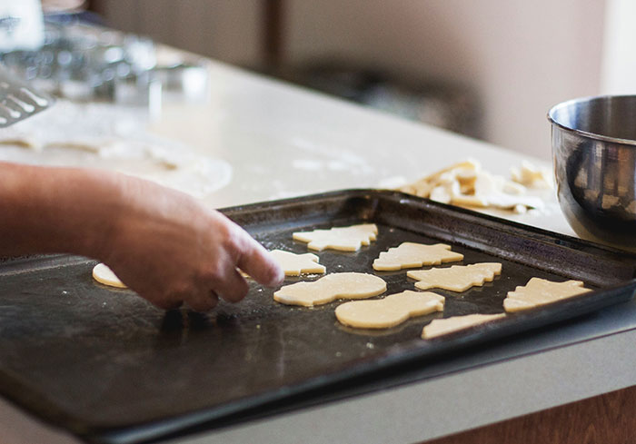 Hand placing cookie shapes on a baking tray, illustrating a normal activity for US citizens.