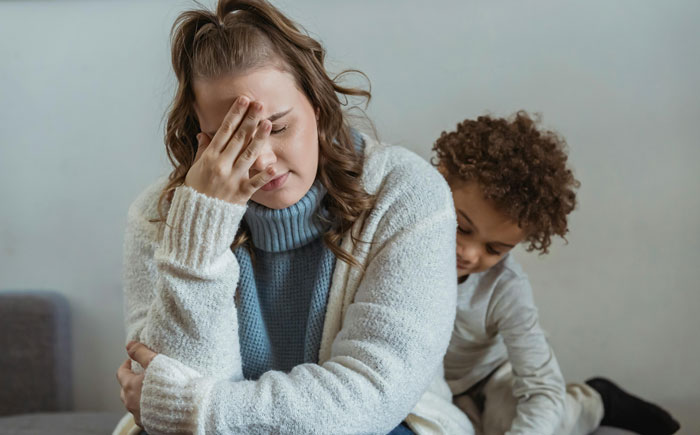 A woman looking stressed on a sofa with a child nearby, related to a nurse hysterectomy appointment.