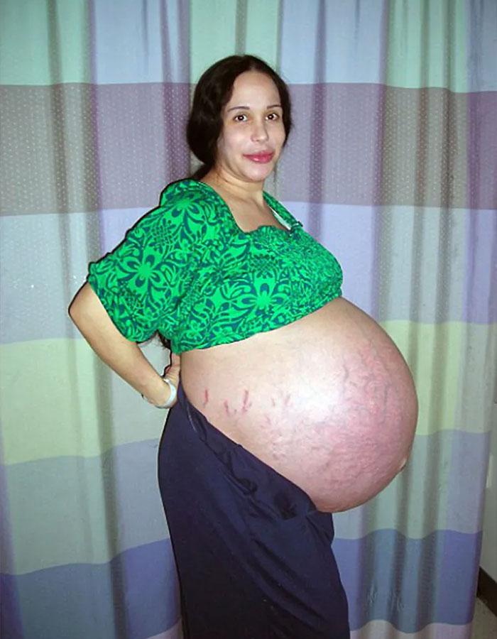 Octomom Nadya Suleman, pregnant with octuplets in 2009, wearing a green shirt and standing sideways against a curtain background.