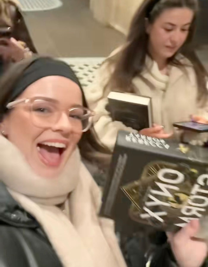 Excited readers at a bookstore holding copies of Onyx Storm Craze, capturing the buzz similar to Harry Potter launches.