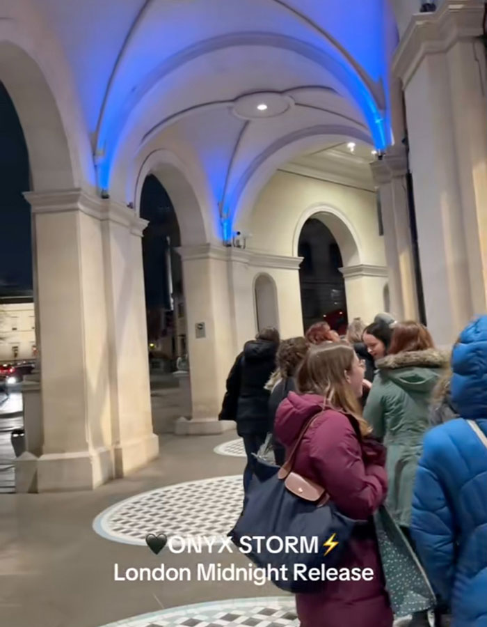 People line up under arches in coats for the Onyx Storm book midnight release in London.