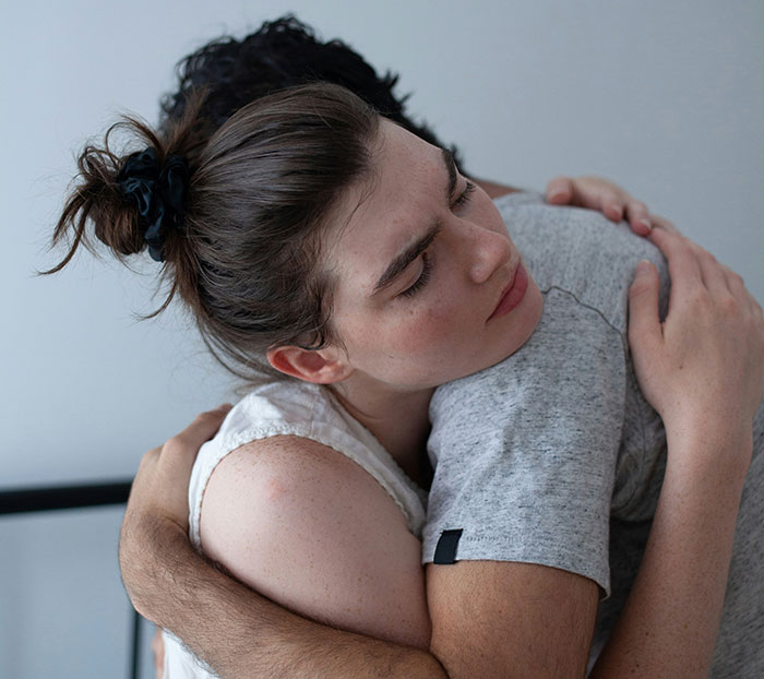 A woman with a solemn expression receiving a comforting hug, conveying emotional support.