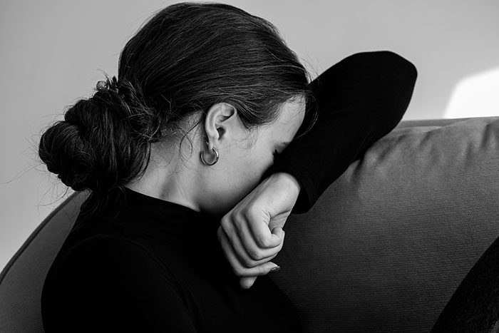 A woman in distress, sitting on a couch, covering her face with her arm, showing emotion related to a miscarriage.