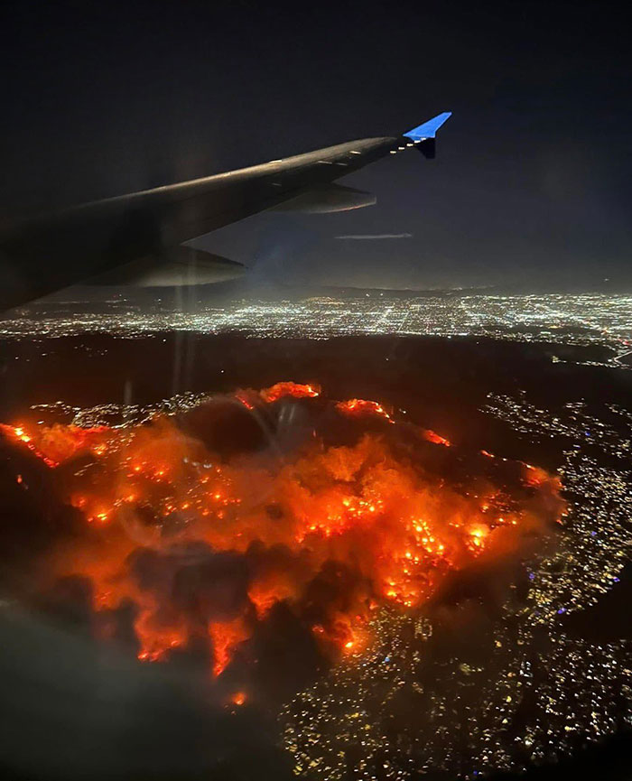 Aerial view of LA fires at night, city lights visible, highlighting wildfire impact.