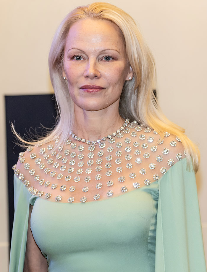 Blonde woman in an elegant green dress with floral embellishments, showcasing a makeup-free look at a formal event.