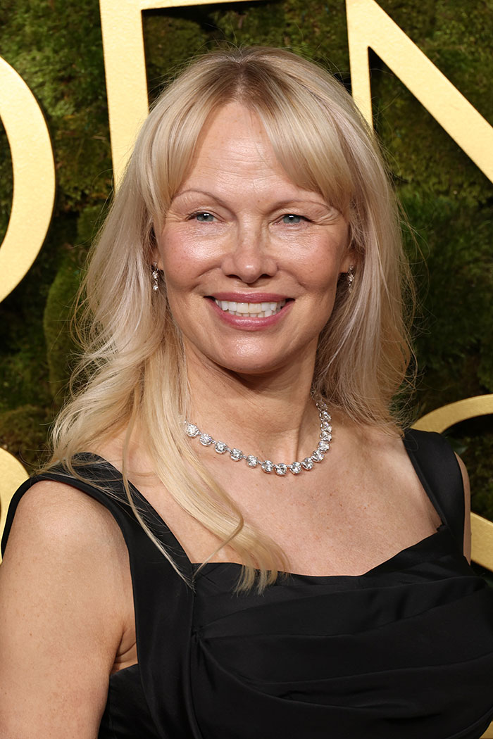 Makeup-free look at the 2025 Golden Globes featuring a woman in a black dress, smiling gracefully on the red carpet.