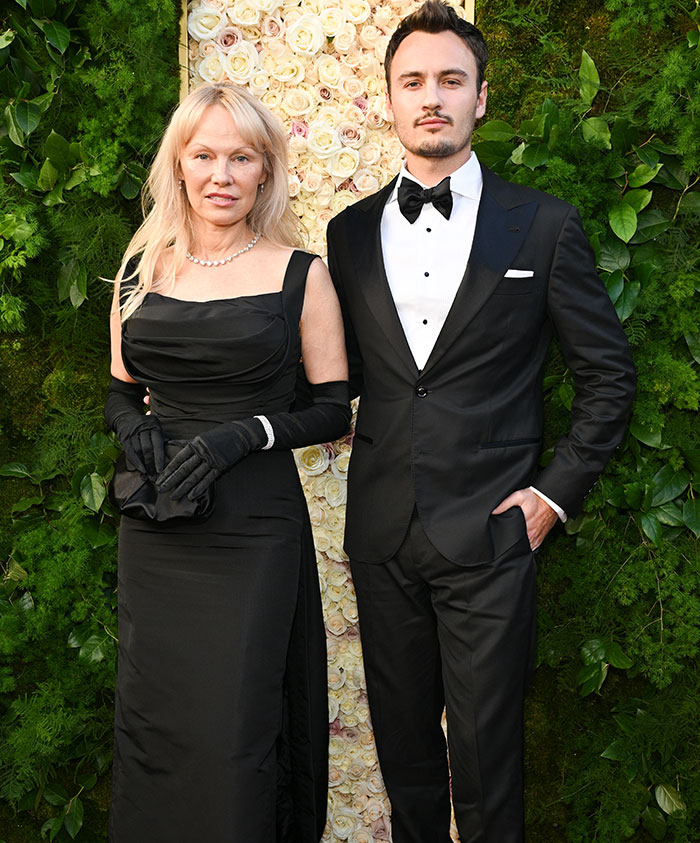 Two people in formal attire at a garden event, highlighting a makeup-free look that sparks debate.