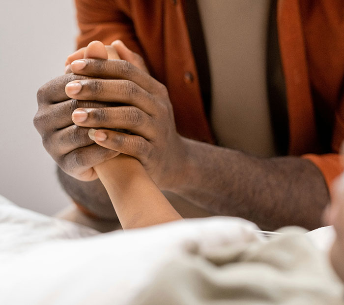 A comforting hand holds a child's hand in a hospital bed after a sleepover prank accident.