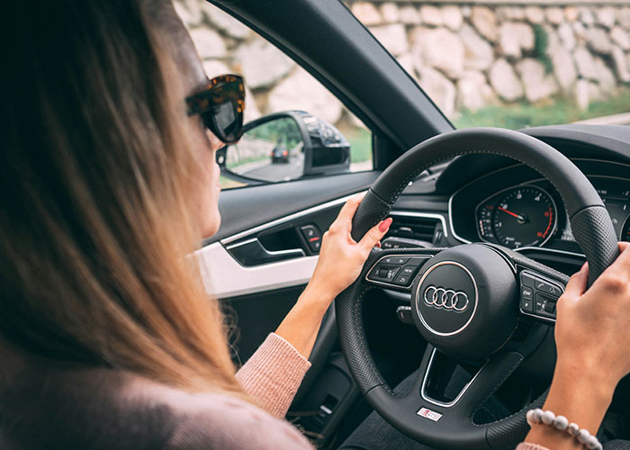 Woman driving an Audi, showing driveway parking concept with focus on car interior.