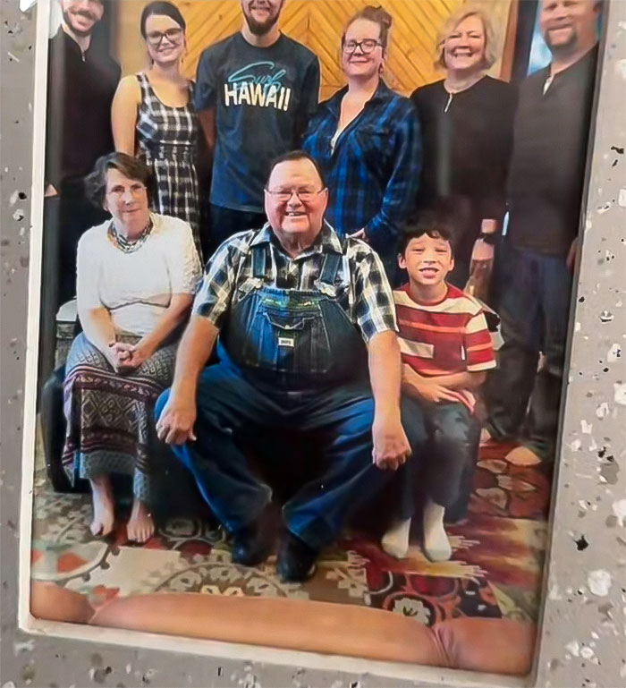 Family portrait with mom and sons posing, surrounded by relatives in a cozy indoor setting.