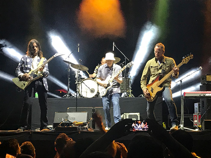 Musicians performing on stage with dynamic lighting and a crowd watching.