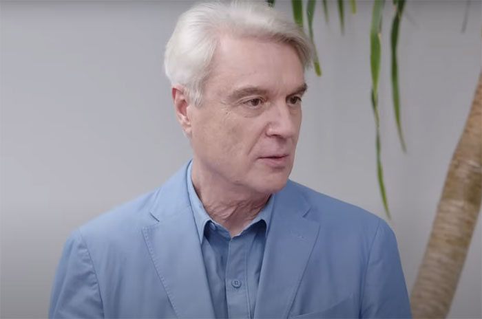 Man in a blue suit standing indoors, unaware he's meeting a famous person.