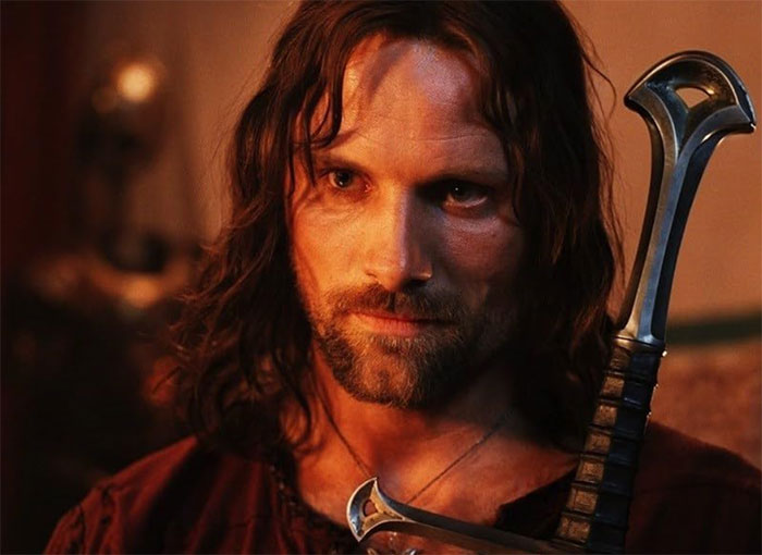 A person in medieval attire holding a sword, with long hair and a focused expression.