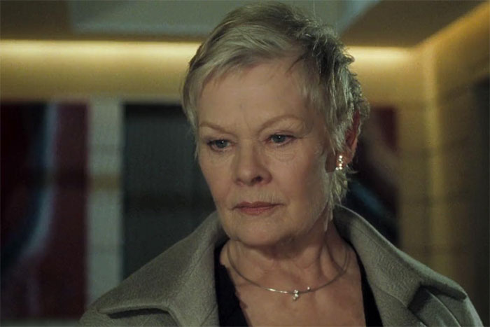 Older woman with short hair, wearing a coat, looking thoughtful indoors; unrevealed famous person.