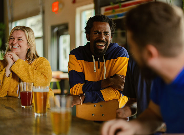 Group of friends laughing and chatting at a bar, drinks on the table, capturing social moments.